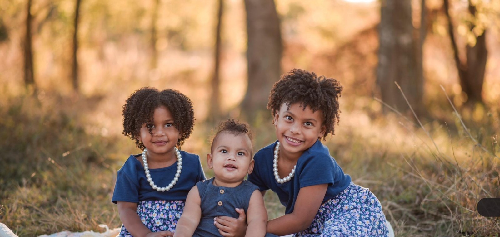 Asher sitting between his two big sisters in a field at sunset